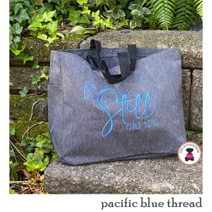 May include: A gray tote bag with black handles and the words "Be Still Psalm 46:10" embroidered in blue thread.