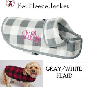 May include: A gray and white plaid pet fleece jacket with the name "Lilly" embroidered in pink. The jacket has a gray trim and is designed for a dog. The image also shows a dog wearing a red and black plaid jacket.