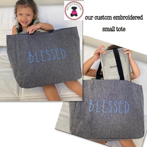 May include: Gray tote bag with the word "BLESSED" embroidered in blue. The tote bag is shown in two different photos. In the first photo, a young girl is holding the tote bag. In the second photo, the tote bag is shown with a book inside.