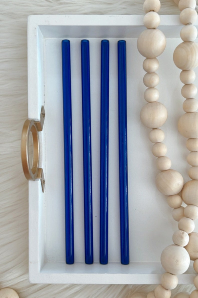 Pu&ograve; includere: Cinque cannucce da bere in vetro blu in un vassoio bianco. Le cannucce sono disposte in fila, con le estremit&agrave; delle cannucce allineate. Le cannucce sono lunghe circa 25 cm.