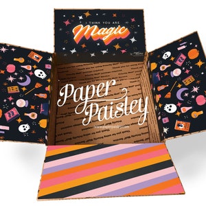May include: An open cardboard box with a black and white patterned interior. The box is decorated with a Halloween theme, featuring stars, moons, pumpkins, and potion bottles. The top flap of the box has a black background with white stars and the text "I think you are magic" in a colorful retro font.