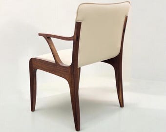 May include: A white leather armchair with a wooden frame. The chair has a curved back and arms, and the legs are tapered.