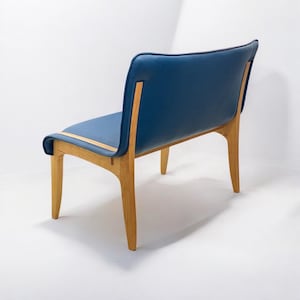 May include: A modern chair with a navy blue seat and backrest. The chair has a wooden frame and legs, with a light-colored wood accent on the seat. The design is minimalist and elegant, suitable for a living room or dining area.