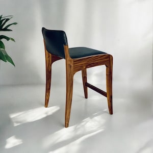 May include: A dark wood bar stool with a black leather seat. The stool has a simple, modern design with a curved back and a slightly angled seat.