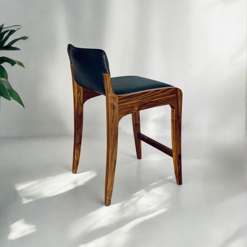 May include: A dark wood bar stool with a black leather seat. The stool has a simple, modern design with a curved back and a slightly angled seat.