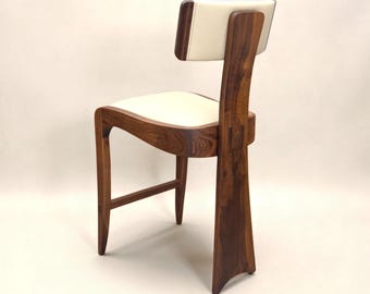 May include: A chair constructed from dark brown wood with a curved frame and a cream-colored upholstered seat and backrest. The design features a tall, wide rear leg that supports the backrest, with a single horizontal footrest between the front legs.