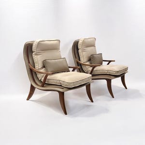 May include: Two beige upholstered chairs with wooden frames and curved legs. The chairs have a high back and a thick cushion.
