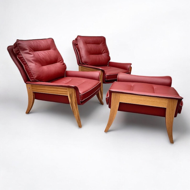 May include: Two red leather armchairs with wooden frames and a matching red leather ottoman with wooden legs.