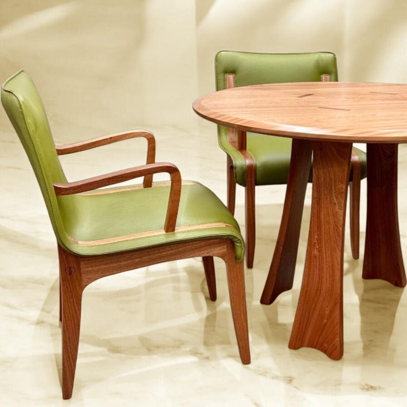 May include: A round wooden table with a natural wood finish and a green leather chair. The table has a unique, curved base and the chair has a simple, elegant design.