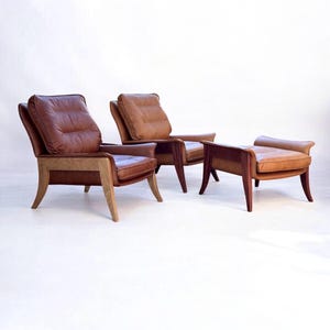 May include: Two brown leather armchairs with wooden frames and a matching brown leather ottoman with a wooden frame.