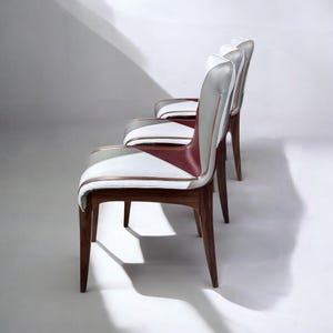 May include: Three chairs with a geometric design on the seat back and seat. The chairs are made of wood and have a white, gray, and burgundy leather upholstery.