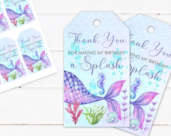 Puede incluir: Etiquetas de agradecimiento con un diseño de cola de sirena. La cola de sirena es morada y rosa con un caballito de mar y burbujas. El texto en la etiqueta dice "Gracias por hacer de mi cumpleaños una salpicadura".