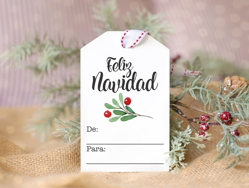 May include: White gift tag with the text "Feliz Navidad" in black cursive script. A small green sprig with red berries is illustrated below the text. The tag has blank lines for "De:" and "Para:" to write the giver and recipient's names.