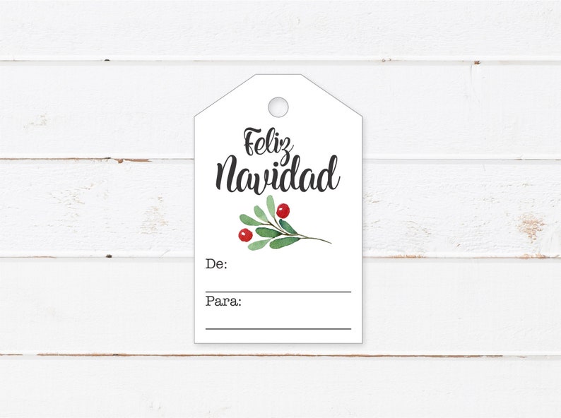 May include: White gift tag with the text "Feliz Navidad" in black cursive lettering. A small green sprig with red berries is below the text. The tag has blank lines for "De:" and "Para:" to write the giver and recipient's names.