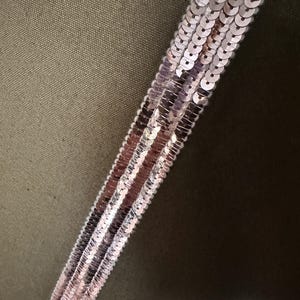 May include: A close-up of a green fabric with a strip of pink sequins sewn on it.