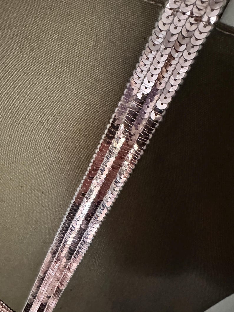 May include: A close-up of a green fabric with a strip of pink sequins sewn on it.