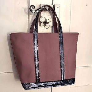 Peut inclure: Un sac cabas mauve avec des bordures en sequins noirs sur les poignées et le bas. Le sac a un design simple et est fait d'un matériau en toile durable.