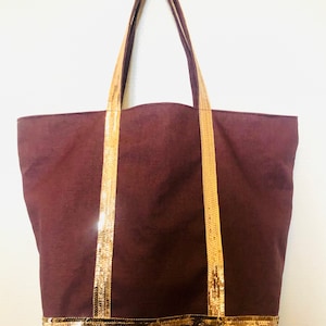 Puede incluir: Una bolsa de lona marr&oacute;n con ribete de lentejuelas doradas. La bolsa tiene dos asas largas y una base ancha.