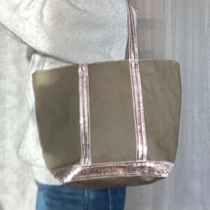 May include: A large, olive green canvas tote bag with pink and white sequined trim. The bag has two long handles.