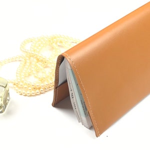 Peut inclure: Une couverture de chéquier en cuir marron avec des coutures blanches. La couverture est fermée et posée sur une surface blanche.