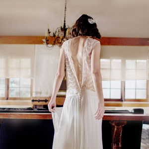 May include: A white lace wedding dress with a low back and a flowing skirt.
