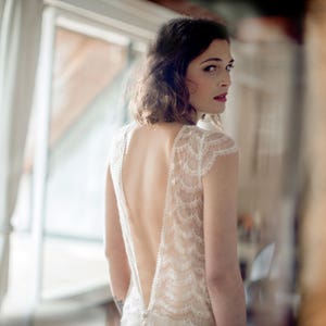 May include: A woman wearing a white lace wedding dress with a low back and a plunging neckline.