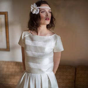 Puede incluir: Una mujer con un vestido de novia blanco con un corpiño de encaje y una diadema de flores blancas. El vestido tiene un corpiño ajustado y una falda completa.