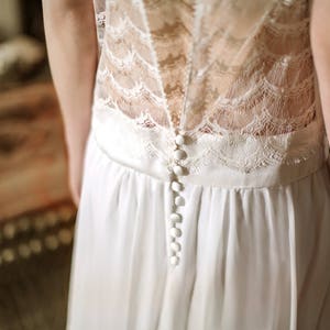 May include: A white lace and chiffon wedding dress with a row of white buttons down the back.