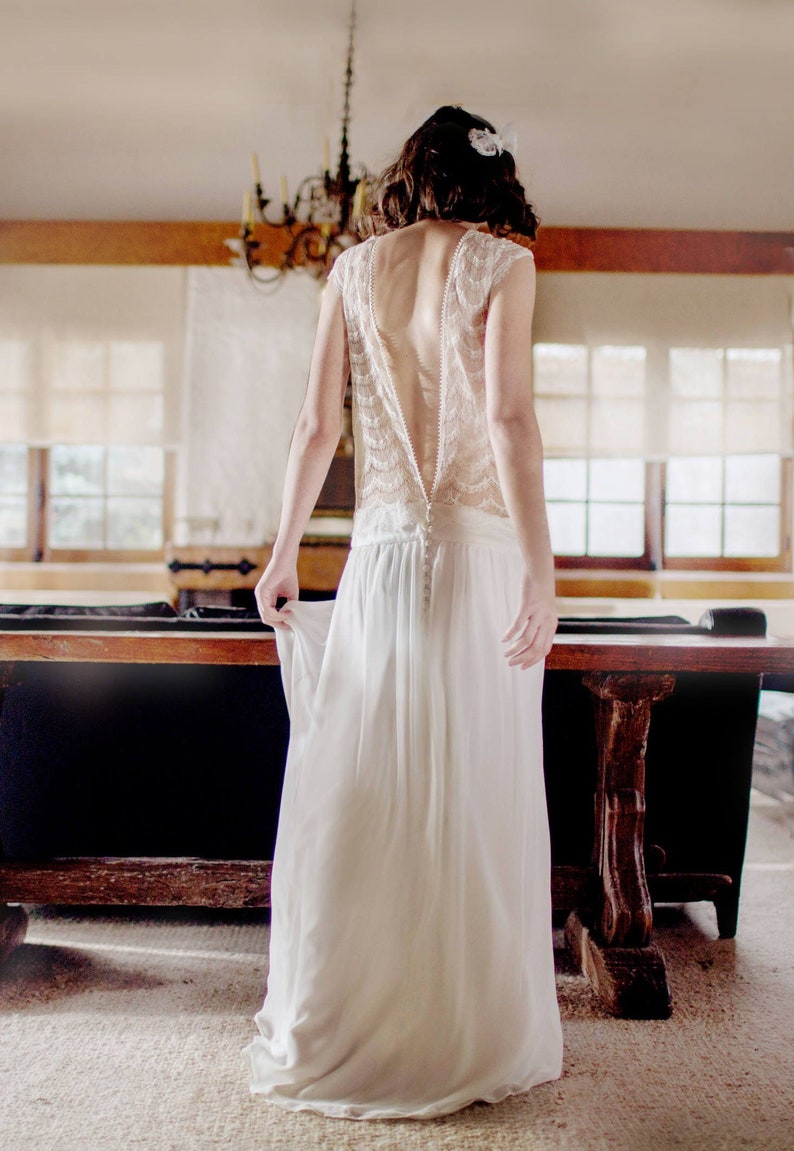 May include: A white lace wedding dress with a low back and a flowing skirt.