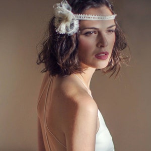 Könnte beinhalten: Eine Frau mit kurzen, welligen braunen Haaren trägt ein weißes Spitzenhaarband mit einem Blumenakzent. Sie trägt ein weißes ärmelloses Kleid mit einem tiefen Rücken.