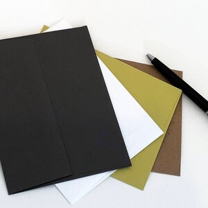 May include: A stack of envelopes in black, white, and green, with a black pen lying on a white surface.