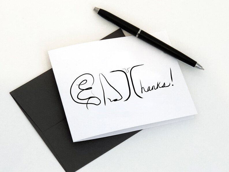 May include: A white card with a black line drawing of a face and the word "thanks!" written in black ink. The card is sitting on a black envelope.