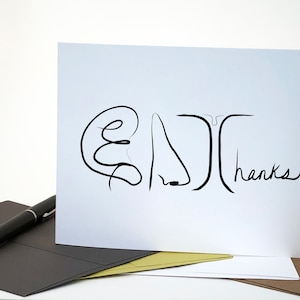 May include: A white card with a black line drawing of a face and the word "thanks!" written in black ink.