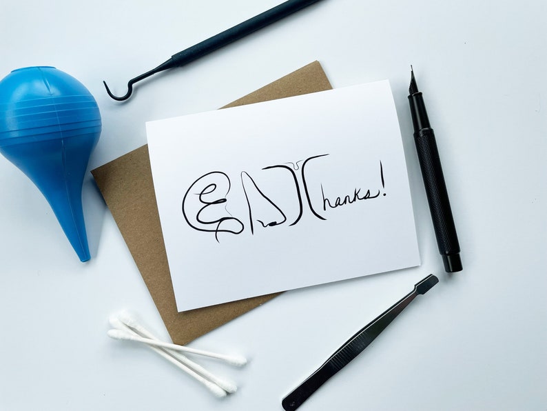 May include: A white card with a black line drawing of an ear, nose, and mouth with the text "Thanks!" written below. The card is on a brown envelope with a blue bulb syringe, a black pen, a black tweezers, and three white cotton swabs on a white surface.