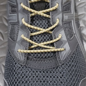 May include: Black athletic shoe with a mesh upper and a yellow and brown shoelace. The shoe has a gray and black design on the side and the word "asics" is visible on the top of the shoe.