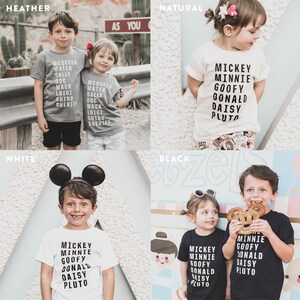 May include: Four children's t-shirts in different colours: heather grey, natural, white, and black. The shirts feature a variety of Disney characters, including Mickey Mouse, Minnie Mouse, Goofy, Donald Duck, Daisy Duck, and Pluto. The text on the shirts reads "Mickey Minnie Goofy Donald Daisy Pluto".