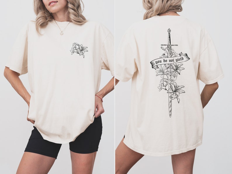 May include: A white oversized t-shirt with a black line drawing of a sword and flowers on the back. The text "you do not yield" is on a banner wrapped around the sword. The front of the shirt has a small black line drawing of flowers on the left side of the chest.
