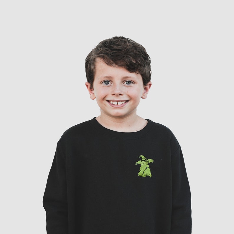 Puede incluir: Sudadera negra con un gr&aacute;fico verde de Oogie Boogie de Pesadilla antes de Navidad. La sudadera de manga larga tiene cuello redondo. El gr&aacute;fico est&aacute; en el pecho izquierdo.