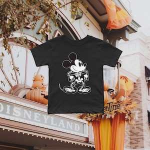 K&ouml;nnte beinhalten: Schwarzes T-Shirt mit einem wei&szlig;en Skelett-Mickey-Mouse-Motiv. Das Shirt ist in Kindergr&ouml;&szlig;e und hat einen Rundhalsausschnitt.