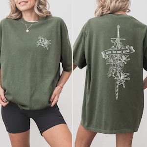 May include: A green t-shirt with a white floral design on the front and a sword with flowers and the text "you do not yield" on the back.