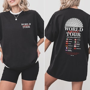May include: Black oversized t-shirt with a graphic print of a globe and the text "WORLD epcot TOUR THE WORLD SHOWCASE" with flags representing different countries. The back of the shirt features a graphic of the Epcot Spaceship Earth.
