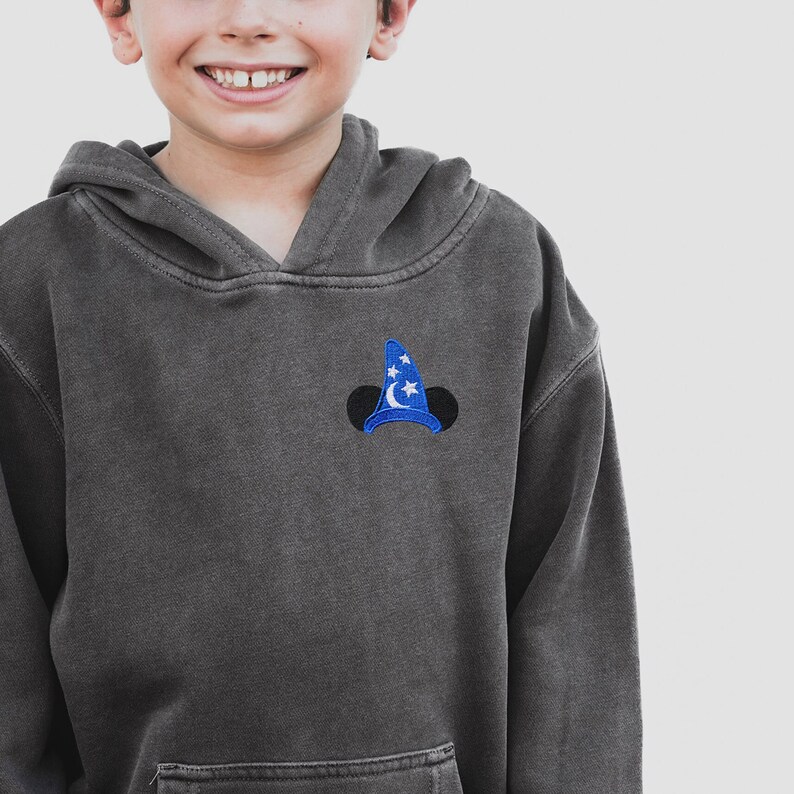 Pu&ograve; includere: Una felpa con cappuccio grigia scura con un cappello da mago di Topolino ricamato in blu e bianco sul davanti.
