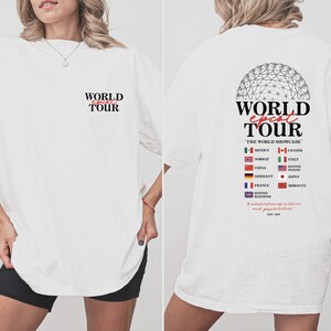 May include: White t-shirt with a graphic of the Epcot World Showcase logo and the text "World Epcot Tour" with flags representing different countries. The text "The World Showcase" is also included. The back of the shirt has the text "World Epcot Tour" with the text "A celebration of cultures and possibilities" and the year "EST 1982".