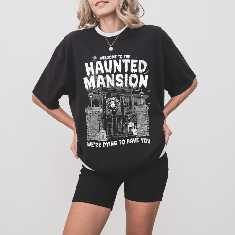 May include: Black t-shirt with a white graphic of a haunted mansion with the text "Welcome to the Haunted Mansion We're Dying to Have You".