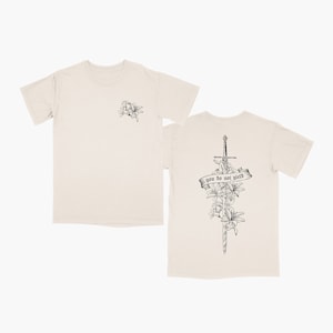 May include: A beige t-shirt with a black and white floral design on the front and a sword with flowers and the text "you do not yield" on the back.