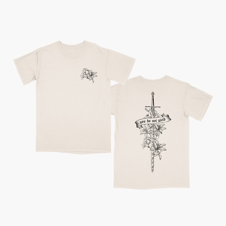 May include: A beige t-shirt with a black and white floral design on the front and a sword with flowers and the text "you do not yield" on the back.