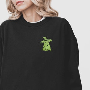 Puede incluir: Sudadera negra con un peque&ntilde;o bordado verde del personaje Oogie Boogie en el pecho. La sudadera tiene cuello redondo y mangas largas. Se ve una camiseta interior blanca en el cuello. El dise&ntilde;o est&aacute; inspirado en la pel&iacute;cula "Pesadilla antes de Navidad".