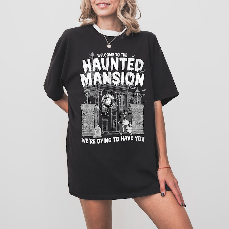 May include: Black t-shirt with a white graphic of a haunted mansion with the text "Welcome to the Haunted Mansion We're Dying to Have You".