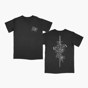 May include: Black t-shirt with a white floral design on the left chest and a white sword with flowers and the text "you do not wield" on the back.