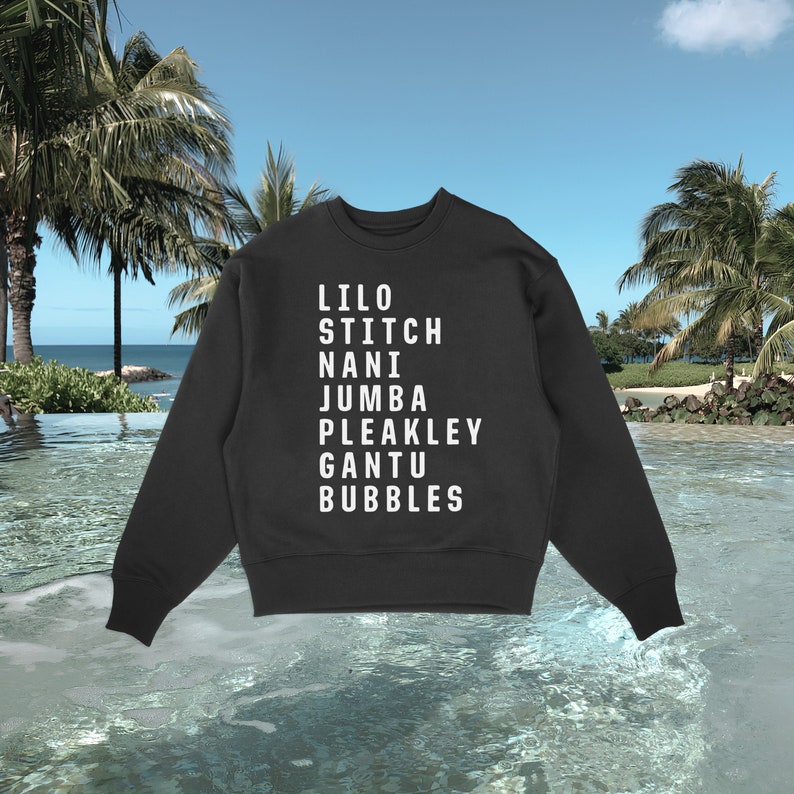 K&ouml;nnte beinhalten: Schwarzes Sweatshirt mit Rundhalsausschnitt und wei&szlig;em Text mit den Namen: Lilo, Stitch, Nani, Jumba, Pleakley, Gantu und Bubbles. Das Sweatshirt wird vor einem tropischen Strandhintergrund mit Palmen und Meer gezeigt.
